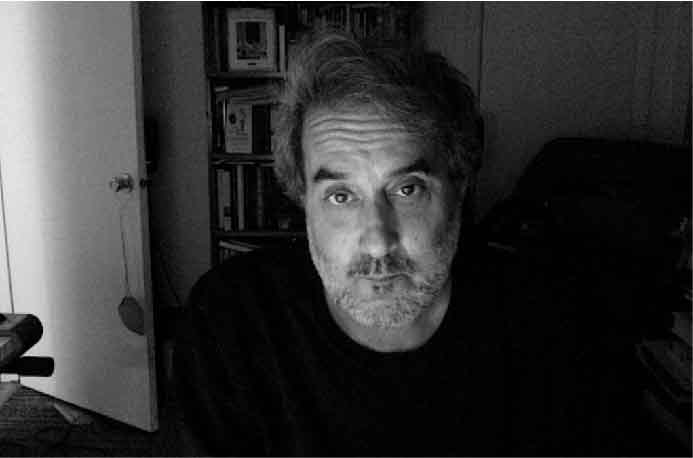 A black and white headshot of Phil Solomon, a white man in his late 50s. Sporting a neatly trimmed goatee and a full head of hair, he is looking seriously into the camera. The photograph appears to have been taken in his home office, adding a personal touch to the image.